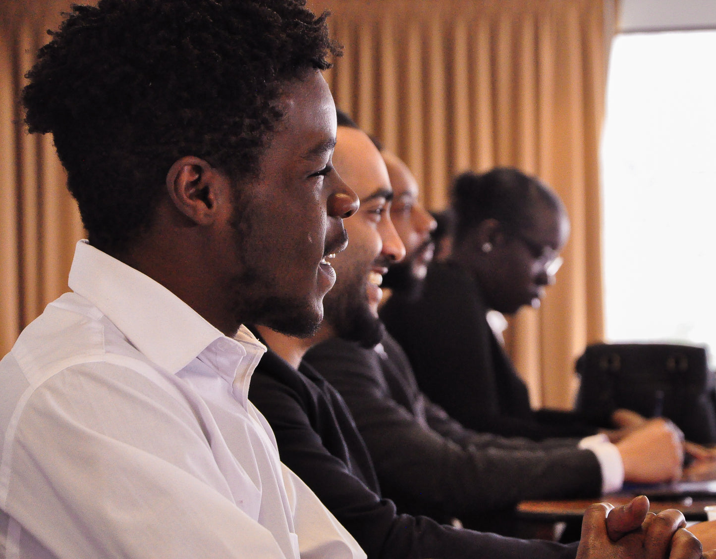 Diverse team at a conference photo of three colored males with a female at the end of the photo out of focus. The first two males are in focus. Everyone dressed in black and white formal attire